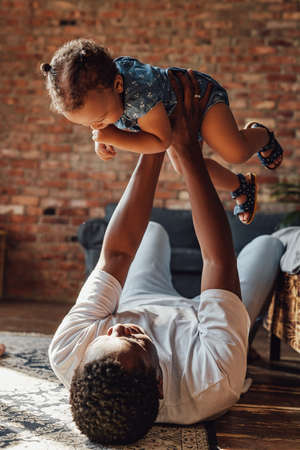 Loving father holding his daughter lying on floor inside roomの写真素材