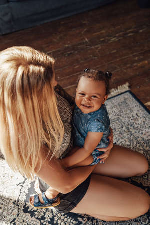 Caring mother embracing her little daughter inside living roomの写真素材