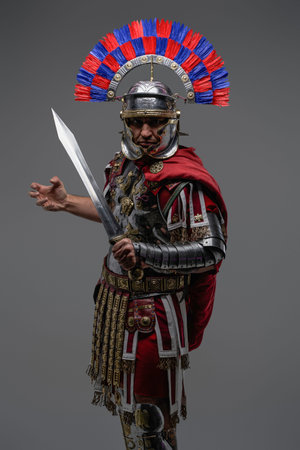 Proud roman soldier posing against gray background holding swordの写真素材