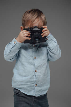 Cheerful child photographer with camera against gray backgroundの写真素材