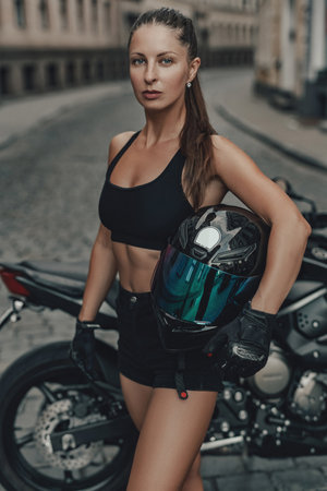 Attractive woman motorcyclist and her black bike in alleyの写真素材