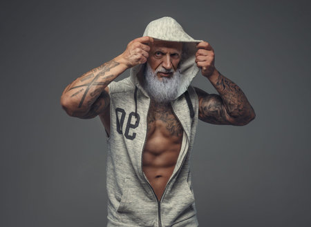 Muscular old man dressed in gray hoody against gray backgroundの写真素材