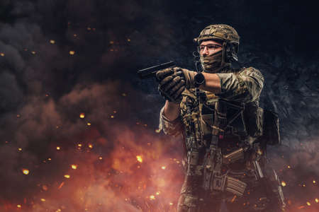 Special force soldier aiming pistol against explosions and fireの写真素材