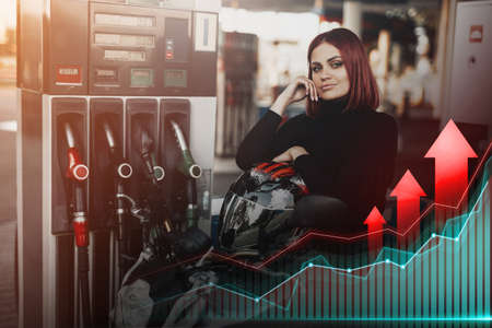 Rise in prices. Redhead woman sitting on motorcycle at gas stationの写真素材