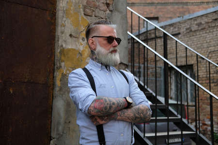 Elegant old man dressed in shirt and pants with suspenders outdoorsの写真素材