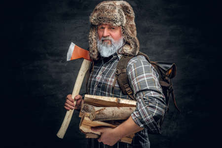 Old man woodman holding hatchet and stack of lumber