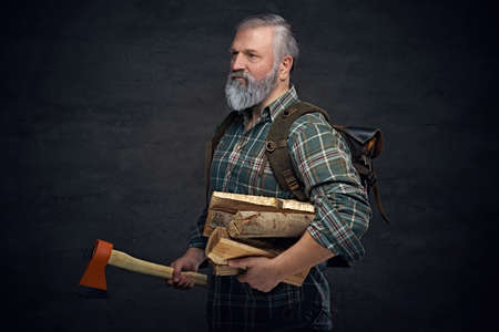 Old man woodcutter holding axe and firewood against dark background
