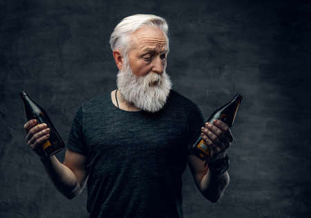 Grandfather with long beard holding two bottles against dark backgroundの写真素材