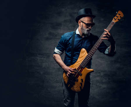Cool elderly hipster guitarist playing guitar against dark backgroundの写真素材