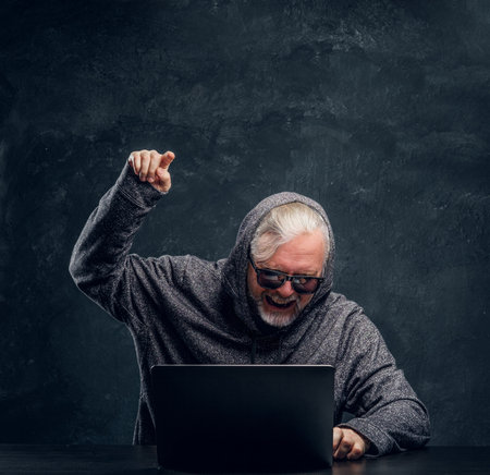 Angry old man hacker with laptop against dark backgroundの写真素材