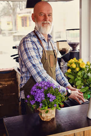 Bearded elderly barista working in modern coffee shopの写真素材