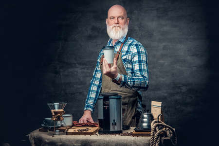 Bald elderly barman holding coffee cup dark background