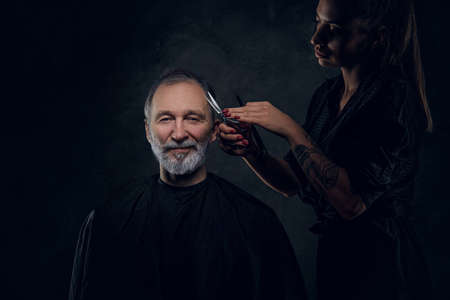 Smiling old man and woman hairdresser cutting his hairsの写真素材