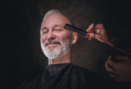 Fashionable senior man cutting his hairs against dark backgroundの写真素材