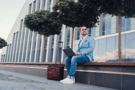 Business person with laptop and baggage sitting on benchの写真素材