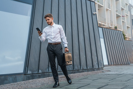 Businessman with bag and cellphone against skyscraperの写真素材