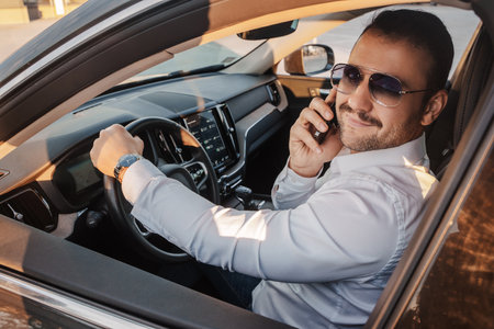 Glad businessperson with cellphone looking at camera inside car