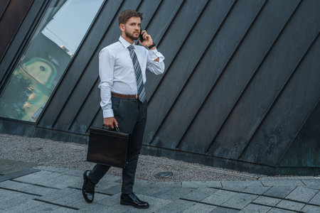 Businessman talking on phone walking around city in daytimeの写真素材