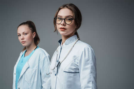 Two female doctors looking at camera against grey backgroundの写真素材