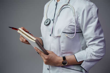 Doctor woman with notebook and pen against grey backgroundの写真素材