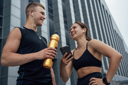 Joyful couple with water bottle and cellphone outdoorsの写真素材