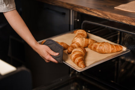 Woman barista baking croissants in coffee bar using stoveの写真素材