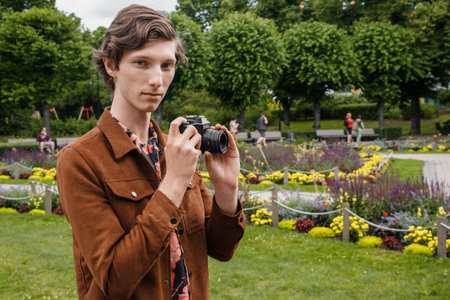 Young guy with photo camera walking in summer public parkの写真素材