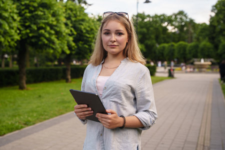 Female student with tablet looking at camera in summer park
