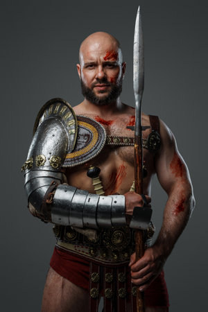 Bearded ancient gladiator with long spear against grey background