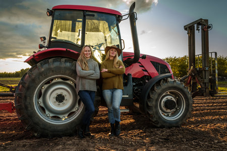 Two women farmers and harvester on cultivated fieldの写真素材