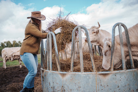 Female farmer with hay on agricultural field with cows