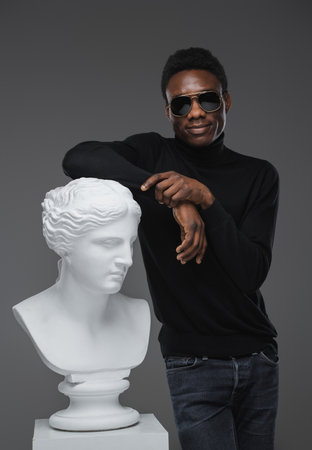 Stylish black guy with greek sculpture against grey backgroundの写真素材