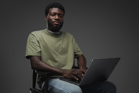 African man typing on laptop sitting on chairの写真素材