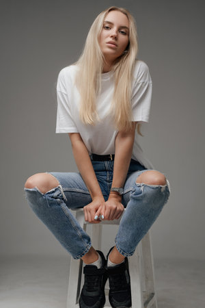 Blond haired beauty posing on chair against gray backgroundの写真素材