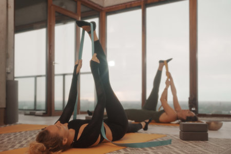 Two girls practicing yoga on a mat using straps