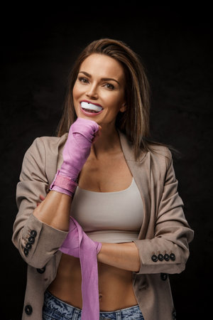 Lively chic sportswoman in jacket and bra showcasing boxing wraps and mouthguardの写真素材