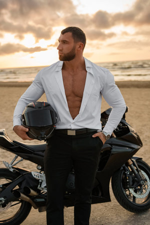 Man with muscular build in an unbuttoned white shirt, leans on his sport bikeの写真素材