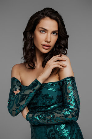 Stunning brunette in a graceful green evening gown against a gray backdropの写真素材