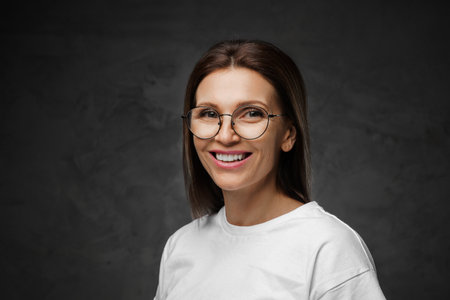 Female in spectacles and white tee beams brightly with a moody backdropの写真素材