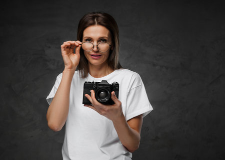Joyful female photographer in spectacles and white tee with her cameraの写真素材