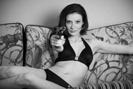young attractive female with a gun on a couchの写真素材