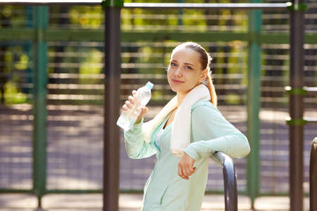 Fitness woman resting after workout, relaxing, drinking clear water from bottle outdoor fitness area in a parkの写真素材