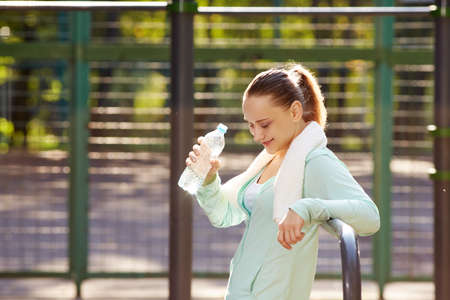 Fitness woman resting after workout, relaxing, drinking clear water from bottle outdoor fitness area in a parkの写真素材