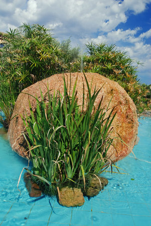 Fountain with a big boulder, decorative reed and a blue sky の写真素材