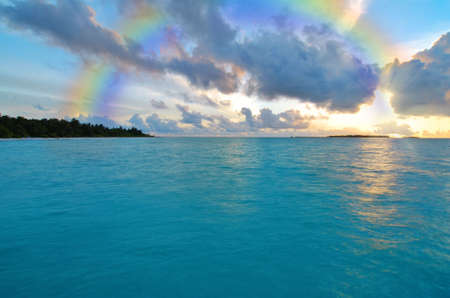 Sunset over ocean and a rainbow in the skyの写真素材