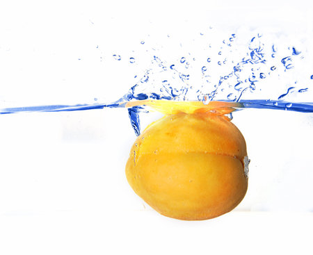 Fresh ripe apricot is falling in the clear blue waterの写真素材