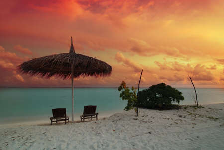 Umbrella and two chairs on the Maldivian beach at beautiful sunsetの写真素材