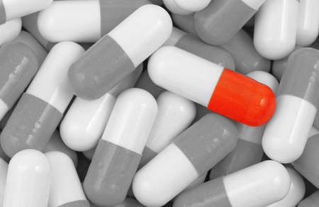 Unique red medical pill in the heap of common balck and white pillsの写真素材
