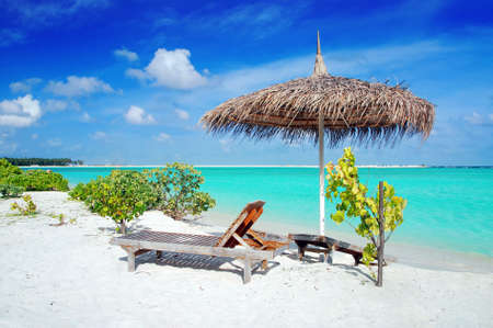 Beautiful Maldivian beach with parasol and two deck chairs in the frontの写真素材