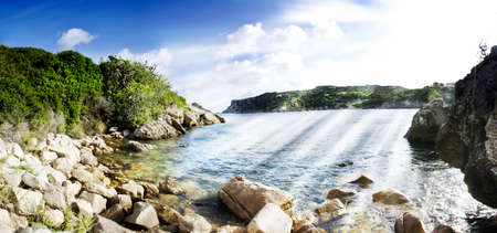 Beach surrounded by rocks with a blue sky. Panoramaの写真素材
